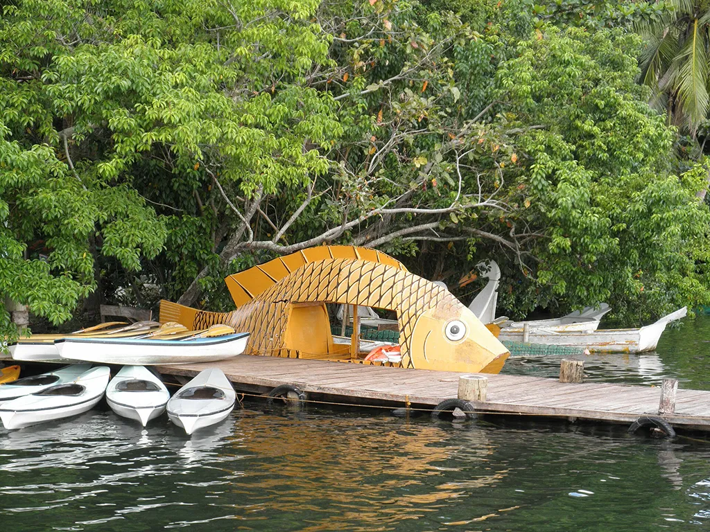 Fish-shaped structure at Danao Lake Camotes Philippines beside wooden dock with kayaks and calm freshwater surrounded by tropical trees.