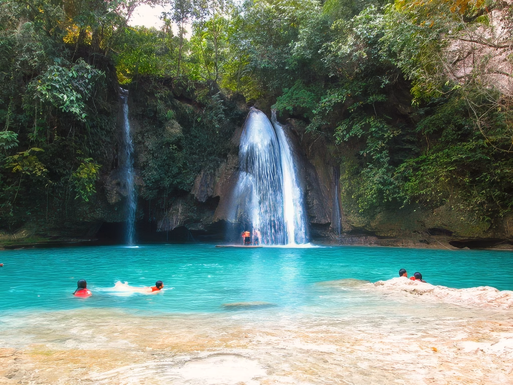 A wide shot of Kawasan Falls’ turquoise waters with people swimming in the foreground.