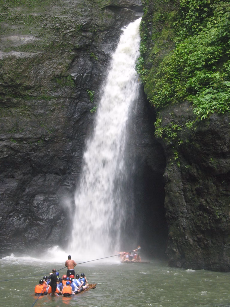 A group of tourists is on a raft moving toward the large Pagsanjan Falls. A second raft is nearly under the falls as well.
