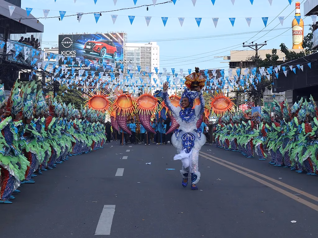 The Bais City contingent performs during the 2025 Sinulog Festival Grand Parade on Maxilom Avenue in Cebu City, Philippines, with a lead dancer in a blue and white sequined costume centered between two lines of performers in coordinated green and blue sea-themed costumes under blue pennant bunting.