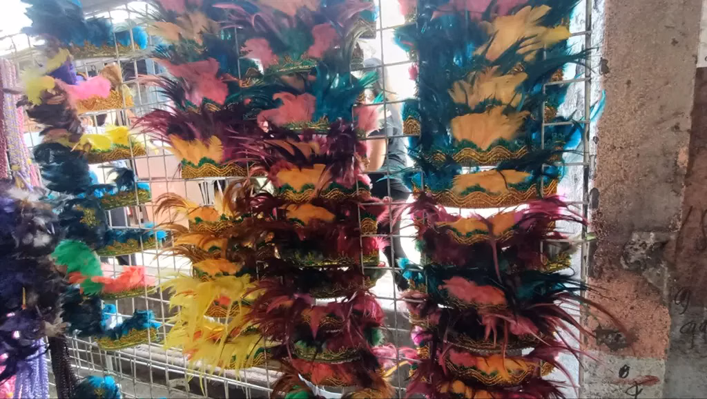 Rows of colorful feathered Sinulog Festival headdresses in teal, pink, burgundy, yellow, and green displayed on wire racks at a Cebu City market stall, available for purchase by festival-goers and parade participants.