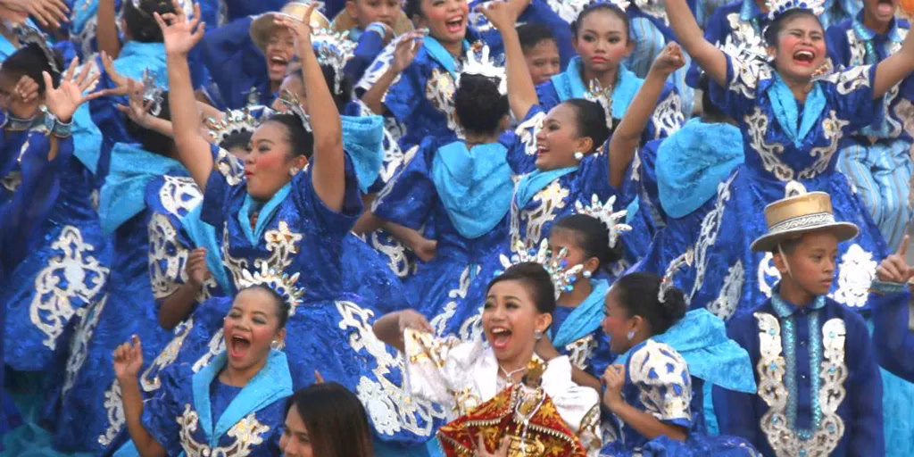 Young performers from the Talisay City Kabataan contingent dancing in elaborate royal blue and gold embroidered costumes during a Philippine festival competition, arms raised and faces expressing pure joy.