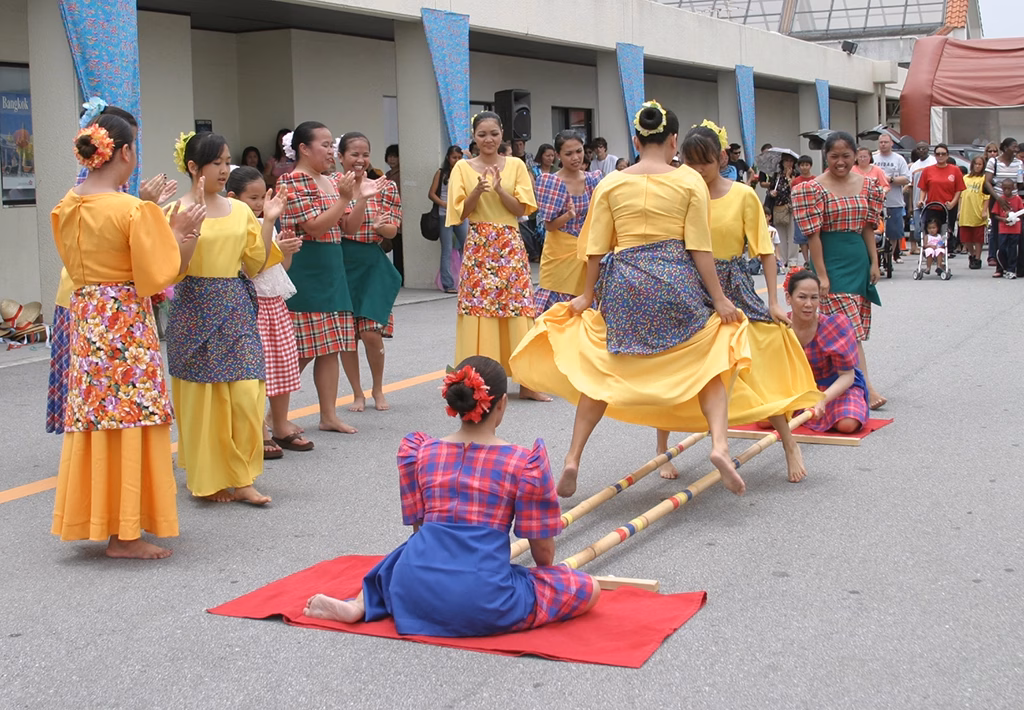 Tinikling dancers leaping between bamboo poles in traditional Filipino clothing.